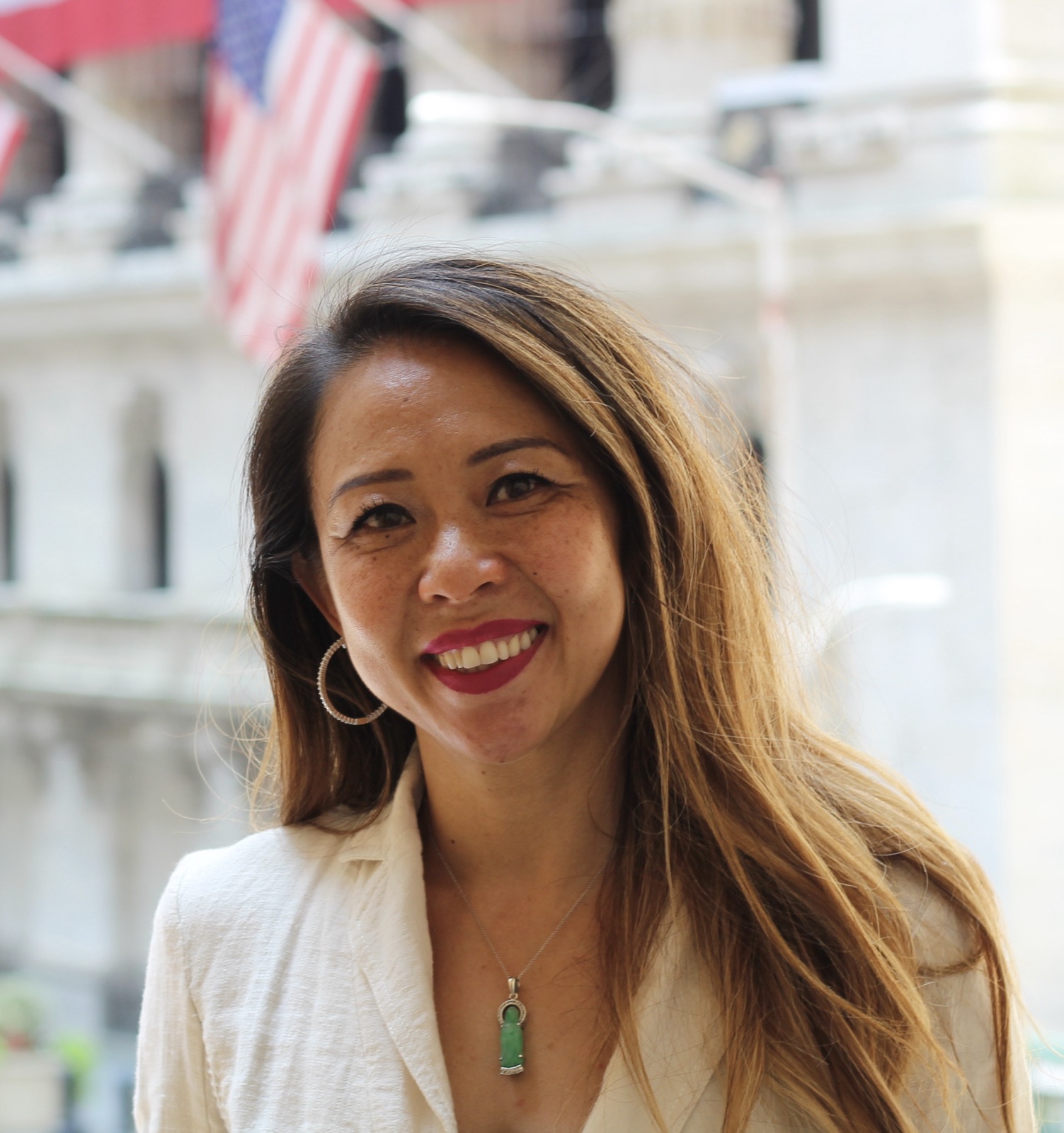 Tammy Nguyen on Wall Street, cream blazer, flags behind her